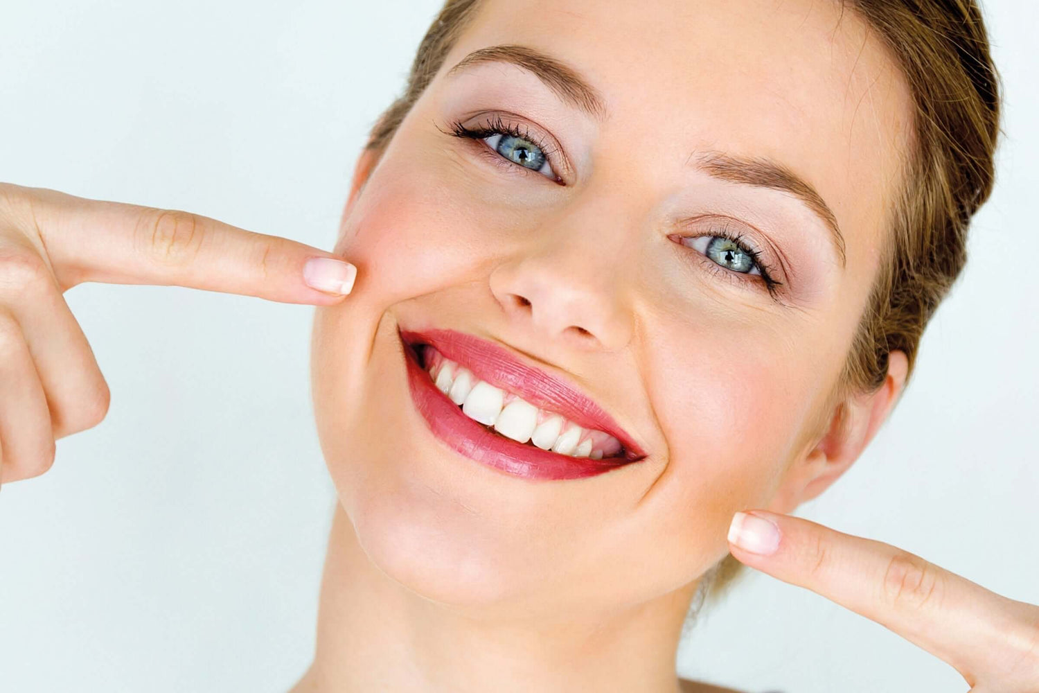 Lächelnde Frau zeigt mit beiden Zeigefingern auf ihre weissen Zähne