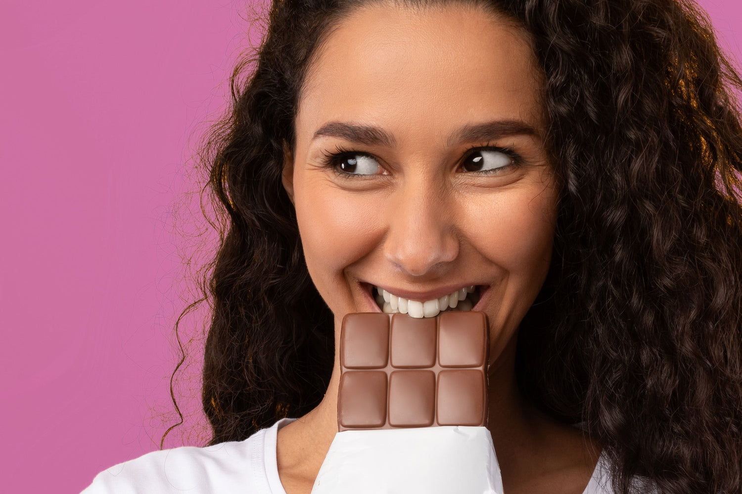 Lachende Frau beisst in Tafel Schokolade