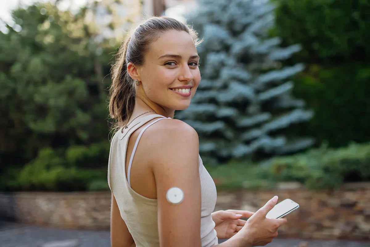 Lächelnde Frau mit Diabetessensor und Smartphone 2