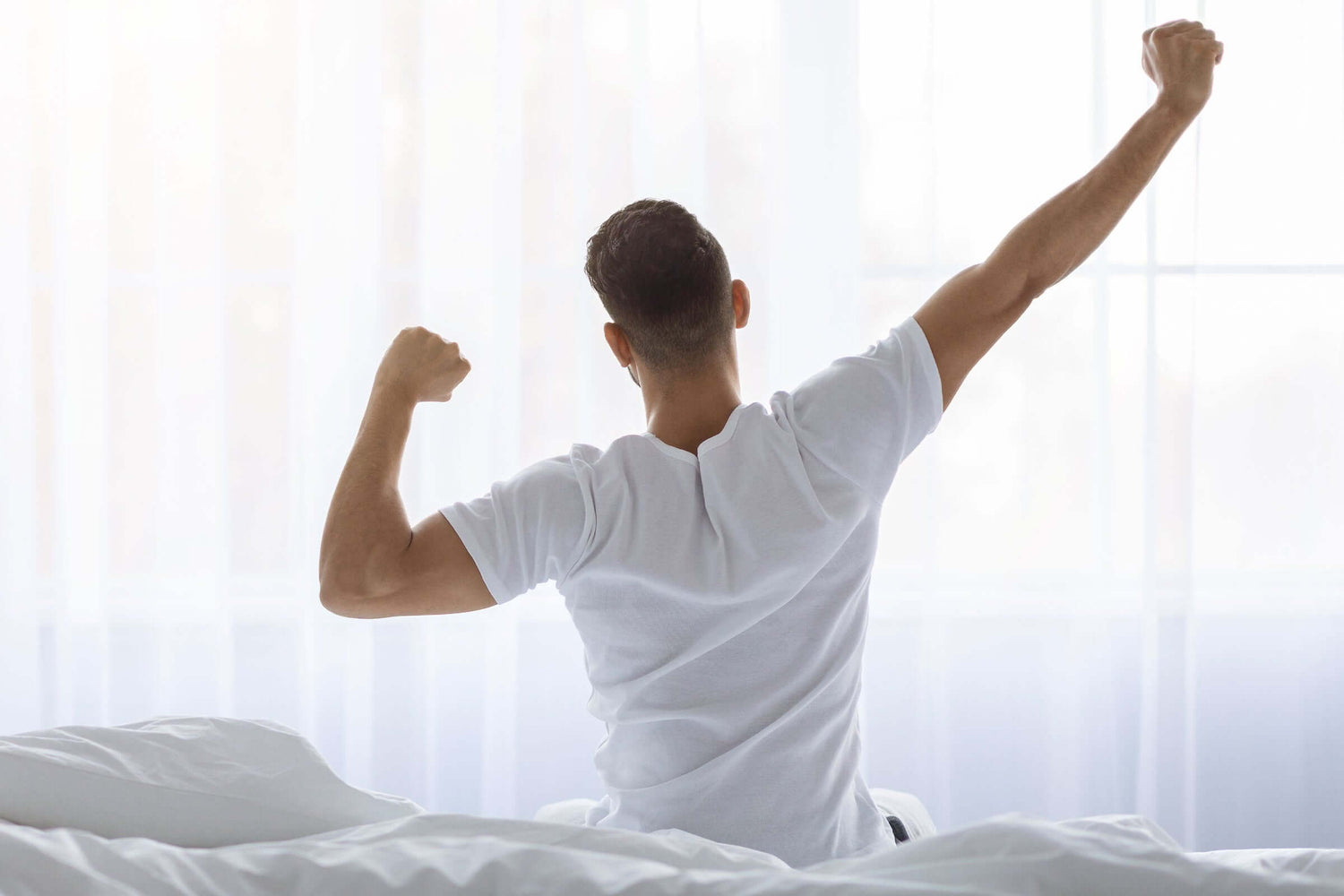 Mann reckt und streckt sich auf dem Bett sitzend