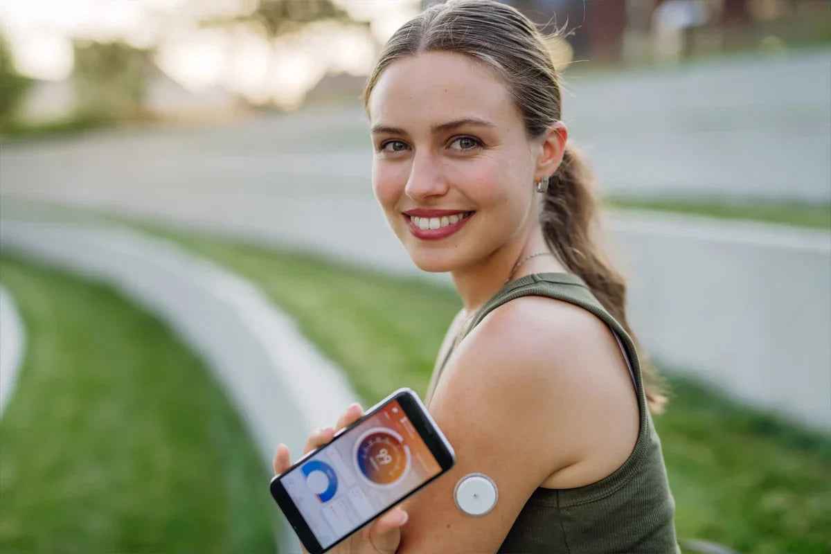 Lächelnde Frau mit Diabetes Sensor und Smartphone
